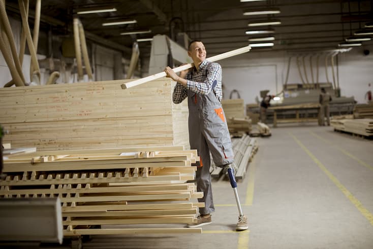 Uśmiechnięty pracownik z protezą nogi niosący drewnianą belkę