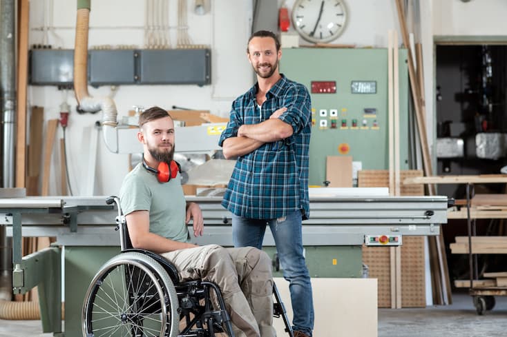 Dwóch uśmiechniętych pracowników, jeden z nich na wózku inwalidzkim